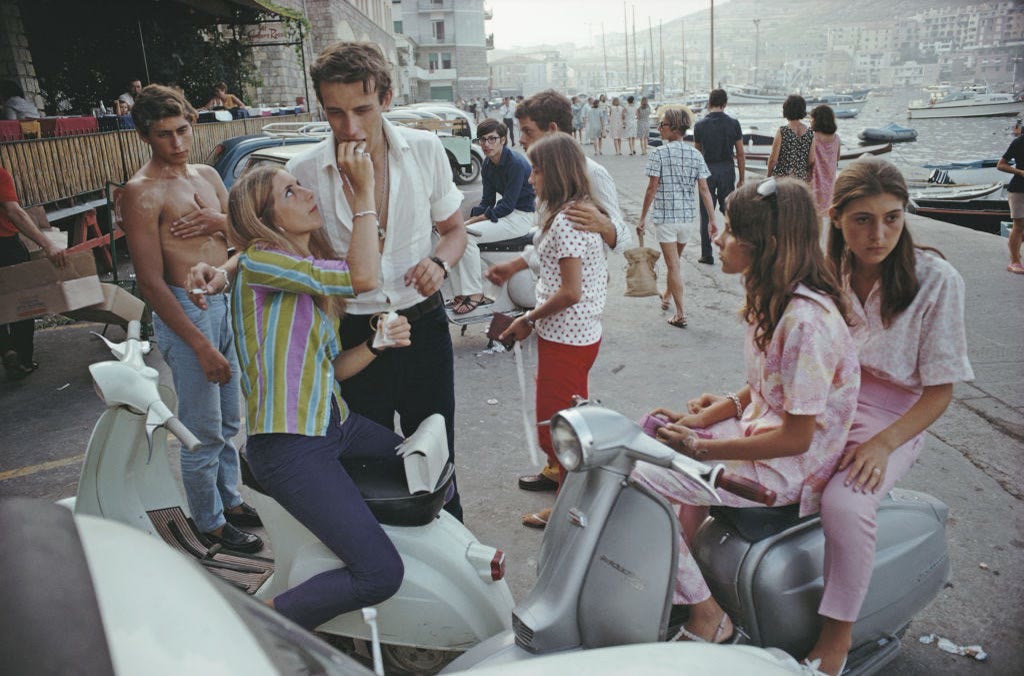 A group of teenagers gathers outdoors with bicycles and scooters.