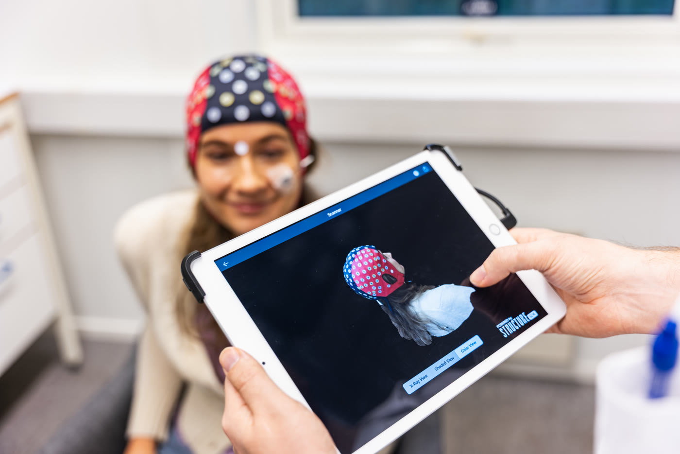 A clinician shows a patient a tablet displaying a color-coded brain image.