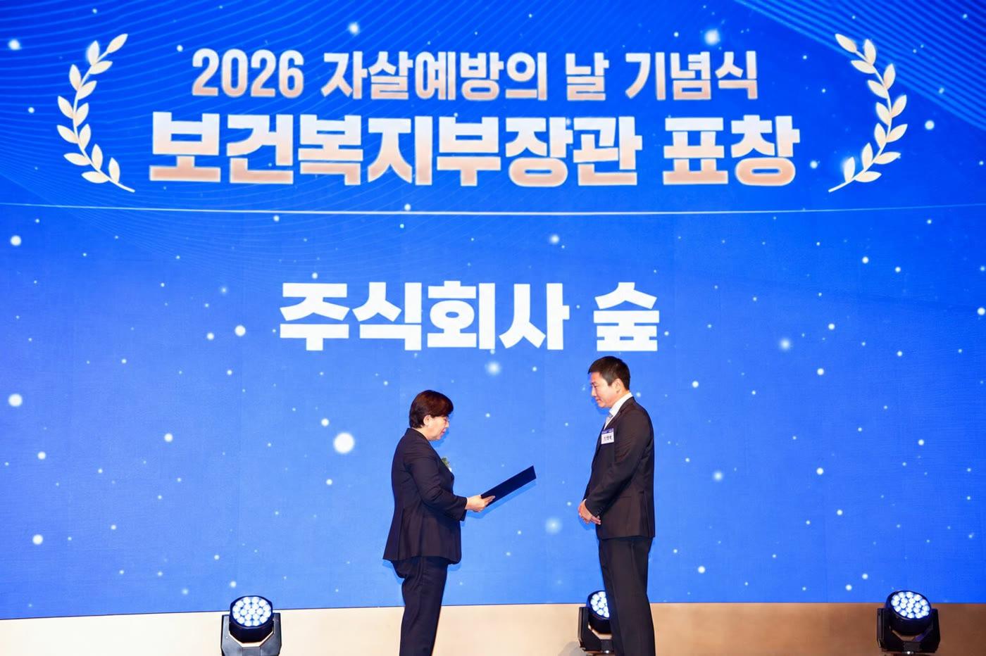 Two people exchange a certificate onstage during a Korean suicide-prevention award ceremony.