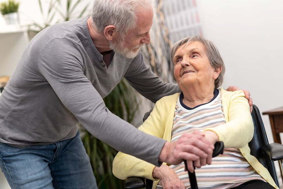 An older adult and caregiver sit together in a home setting.