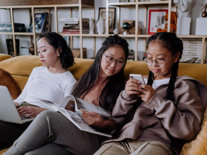 A child uses a smartphone while sitting on a sofa with an adult nearby.