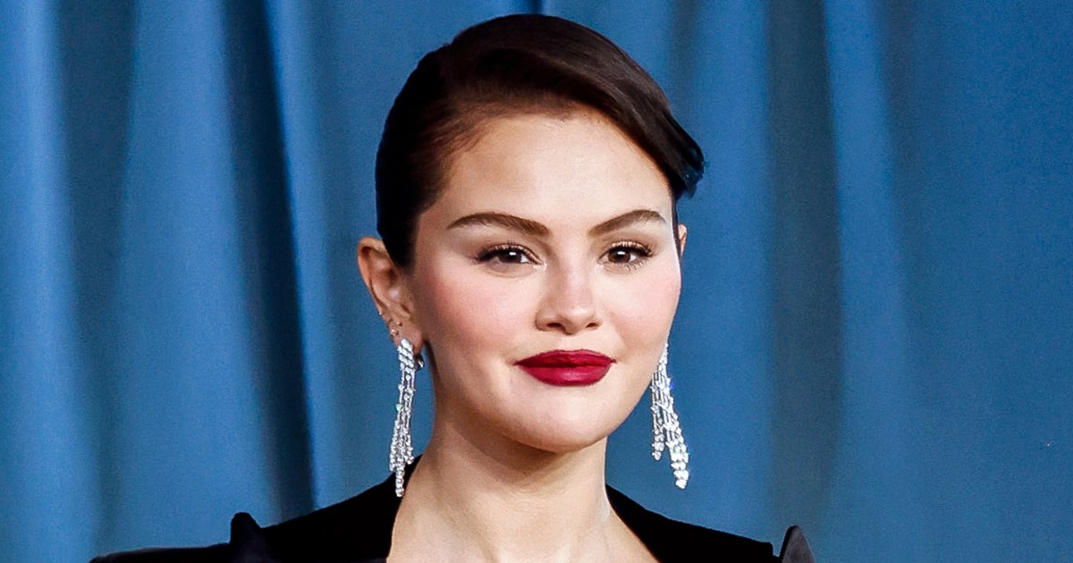Selena Gomez speaking at an event against a dark backdrop.
