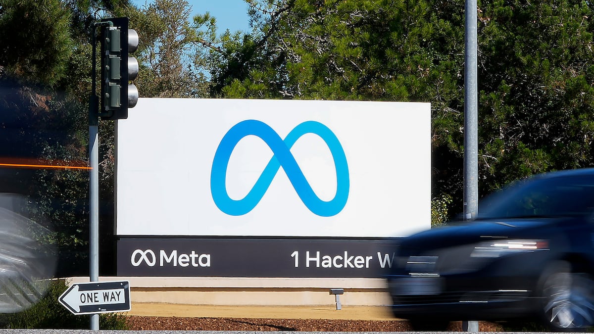 A Meta sign stands beside a road as cars pass in front of trees.