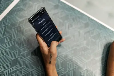 A hand holds a smartphone showing a chatbot screen over a patterned blue-gray surface.