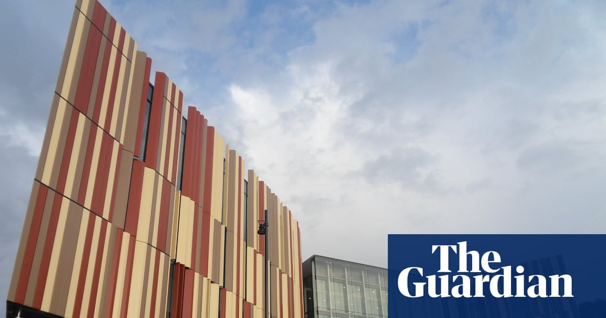 A close view of a university building with red and cream vertical panels beneath a cloudy sky.