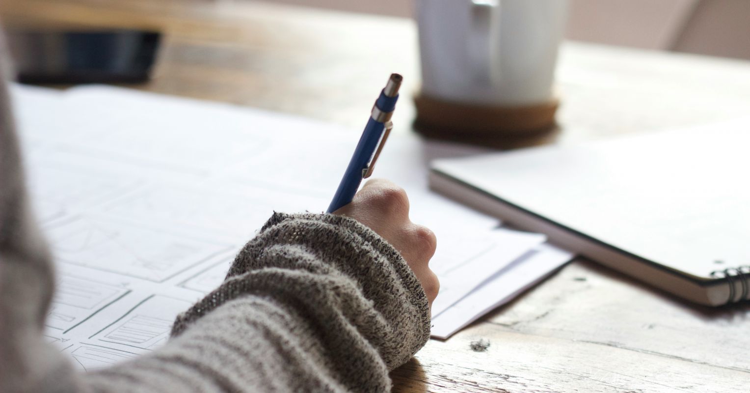 A person writes on a printed form at a table, with a phone and notebook nearby.