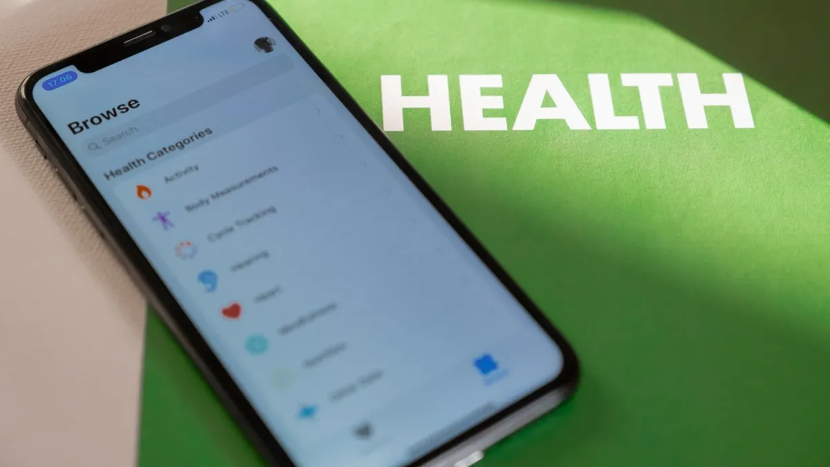 A smartphone displaying health categories rests on a green surface labeled “Health.”