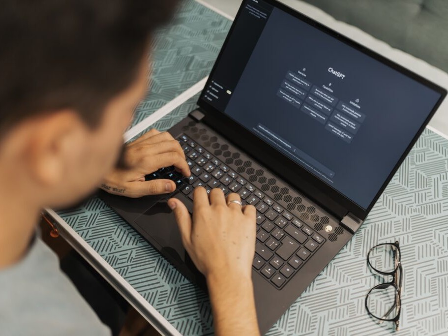A young person types on a laptop displaying the ChatGPT home screen.